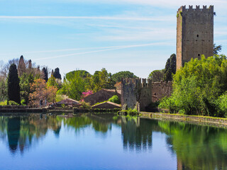 Botanical park, Garden of Ninfa or Giardino di Ninfa near the lake, with medieval castle ruins of Caetani family and various plants. Amazing scenery during spring. Beautiful landscape with blue sky. - obrazy, fototapety, plakaty