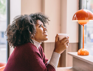 Gorgeous afro woman smiles while enjoying coffee inside a cafe