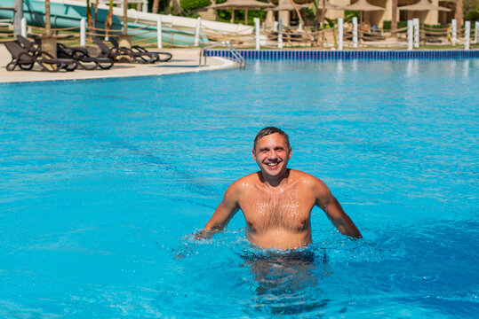 handsome guy half-naked cheerful man smiling laughing in blue water swimming pool. Photo of handsome smiling man in swimming pool in summer scenery