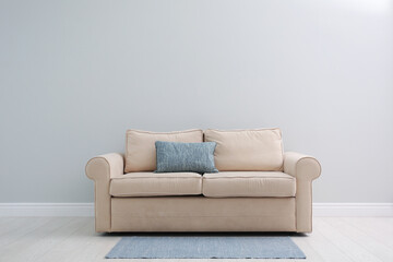 Comfortable beige sofa near light wall indoors, space for text. Simple interior