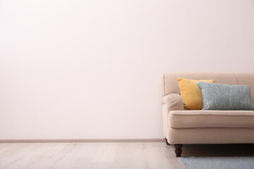 Comfortable beige sofa near light wall indoors, space for text. Simple interior