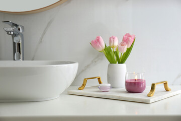 Beautiful flowers and candle on countertop in bathroom. Interior decor