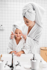 Mother applying face cream on daughter cheeks in bathroom