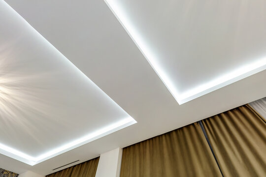 looking up on suspended ceiling with halogen spots lamps and drywall construction in empty room in apartment or house. Stretch ceiling white and complex shape.