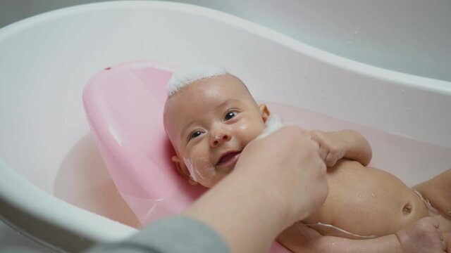 Mom plays with a newborn in the bathroom. The foam from the shampoo on the baby's head