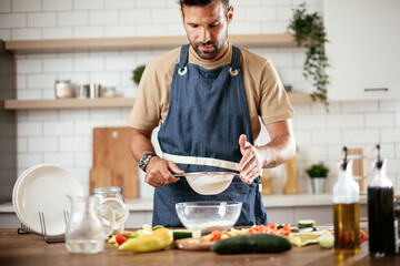 Attractive man cooking in modern kitchen. Handsome man playing with flour while preparing delicious food.