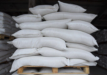 Many bags of sugar are stacked on a wooden pallet, an industrial warehouse.