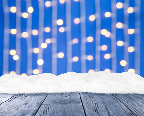 Wooden surface with heap of snow and blurred Christmas lights on background, bokeh effect