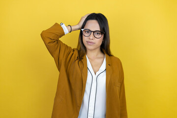 Young beautiful woman wearing a blazer over isolated yellow background putting one hand on her head smiling like she had forgotten something