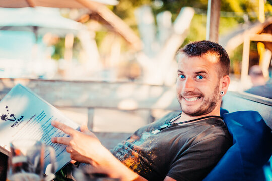 Selective focus shot of a smiling guy with blue eyes and an ear-piercing holding a bar menu