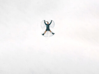 Young beautiful woman in a gray jacket, light pants, boots makes a snow angel in the snow, a view...