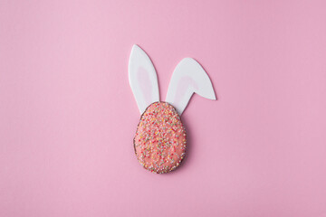 Easter minimalist layout, Easter egg cookie with bunny ears, Easter concept on a pink background, top view