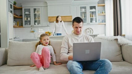 Confident man working on laptop at home, but his daughter disturbing him and pushing keyboard buttons