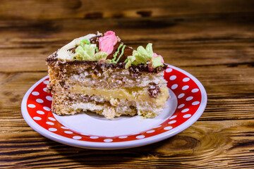 Plate with slice of Kiev cake with cream, nuts and meringue on a wooden table