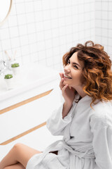 Woman with curly hair smiling and looking away in bathroom