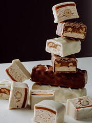 A pyramid of chocolate bars. Closeup of broken chocolate bars with nuts (nougat topped with...