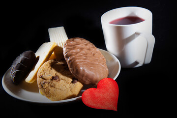 Tea cup of morning drink, waffles, biscuits and red heart on the black background. Romantic breakfast