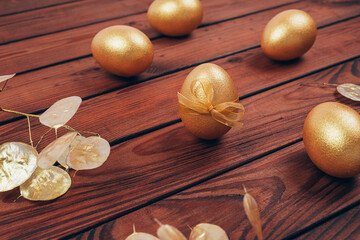 Golden colored Easter eggs with dry flowers over dark wooden planked background. Happy Easter greeting card. Easter wallpaper. 