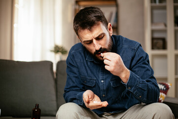 Sick man at home. Young man sitting on sofa having fever.