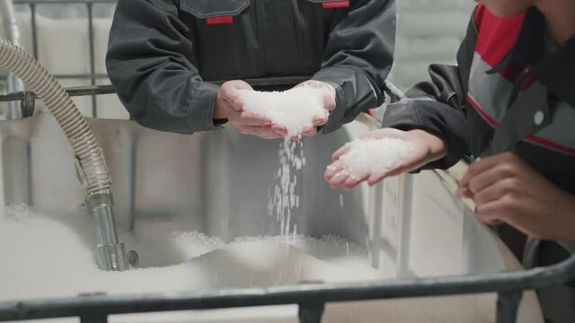 Midsection slow-motion footage of unrecognizable factory workers standing by big container with polypropylene granules holding them in hands and pouring