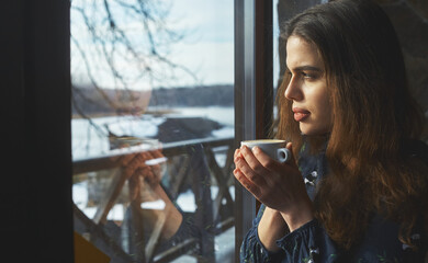 beautiful woman drinking coffee in the morning sitting by the window. view from outside.