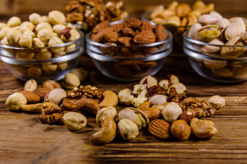 Various nuts (almond, cashew, hazelnut, pistachio, walnut) in glass bowls on a wooden table. Vegetarian meal. Healthy eating concept