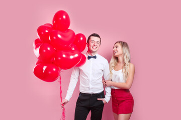 Valentines day. Happy young couple with heart shaped balloons on pink background.