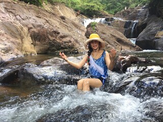 A woman in a yellow hat is climbing a rock in the middle of the river.