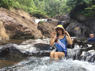 A woman in a yellow hat is climbing a rock in the middle of the river.