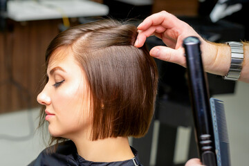 Fototapeta premium A male hairdresser is straightening the hair of the young woman in a beauty salon