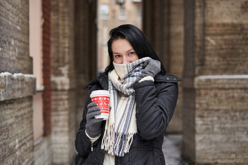 Fototapeta premium beautiful brunette girl hides her nose under a large light scarf on the street in winter
