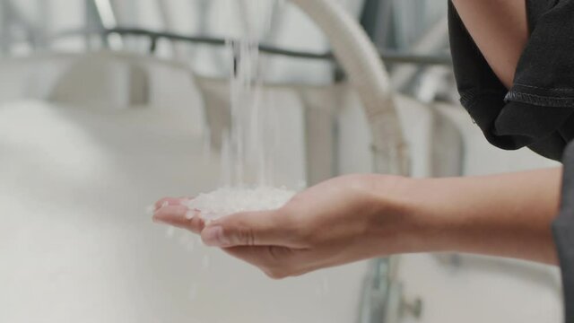 Slowmo close-up of unrecognizable female hands pouring small polypropylene granules at inductrial factory