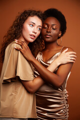 two pretty girls african and caucasian blond posing cheerful together on brown background, ethnicity diverse lifestyle people concept