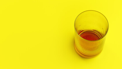 Glass with some cola drink left at bottom on yellow board, space for text left side