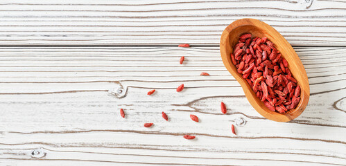 Dried goji aka. wolfberry seeds in wooden bowl and spilled on white boards desk near, view from above