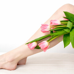 Beautiful slim smooth woman's legs with tulips flowers on white background