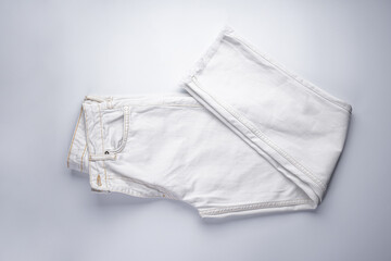White jeans stacked on a gray background, flat lay.