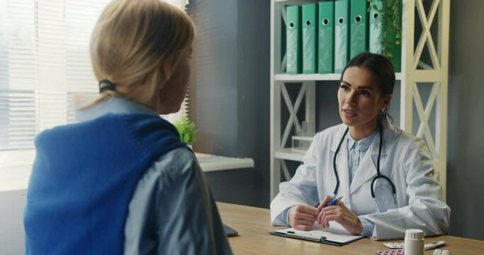Sick woman having appointment with family therapist, describing her health condition. Female doctor listening to patient's disease symptoms and writing medical history.