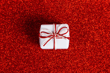 A small white gift on red shiny background, sequins in the side. The concept for Valentine's Day. Copy space.