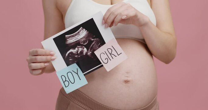 Pregnant woman holding sonography picture with words boy and girl, guessing who is in her belly, close up