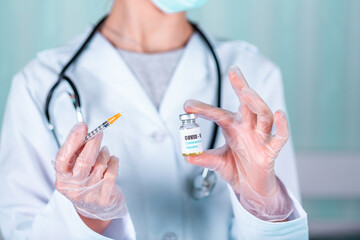 Doctor or nurse in uniform and gloves wearing face mask protective in lab holding medicine vial vaccine bottle with COVID-19 Coronovirus vaccine label