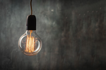 incandescent light bulb with tungsten filaments on old rustic grey concrete wall background. Save...