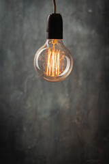 incandescent light bulb with tungsten filaments on old rustic grey concrete wall background. Save...