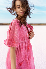 Dreamy woman with clothing eyes and blowy hair posing at pink salt lake. Model in romantic pink...