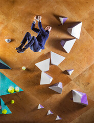 Young man in suit climbing difficult route on artificial wall in bouldering gym. The businessman is happy that he has reached the top.