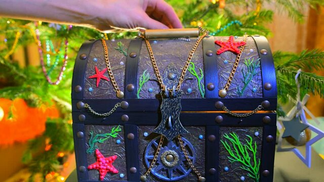 Gift glowing chest on the background of the Christmas tree. Wealth concept for the holiday. A man's hand lays down the currency, francs.