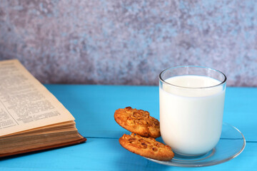 A glass of milk, homemade cakes (oatmeal cookies with nuts) and a book on a blue wooden background.