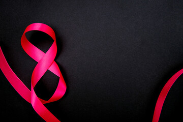 On a black background, a pink satin ribbon in the form of the number eight. Gift wrap.