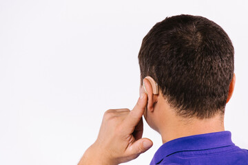 Photo from behind. An enlarged photo. Back of the head of a man pointing at the hearing aid in his ear. White background and empty side ad space.