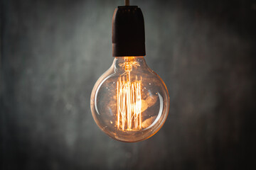 incandescent light bulb with tungsten filaments on old rustic grey concrete wall background. Save...